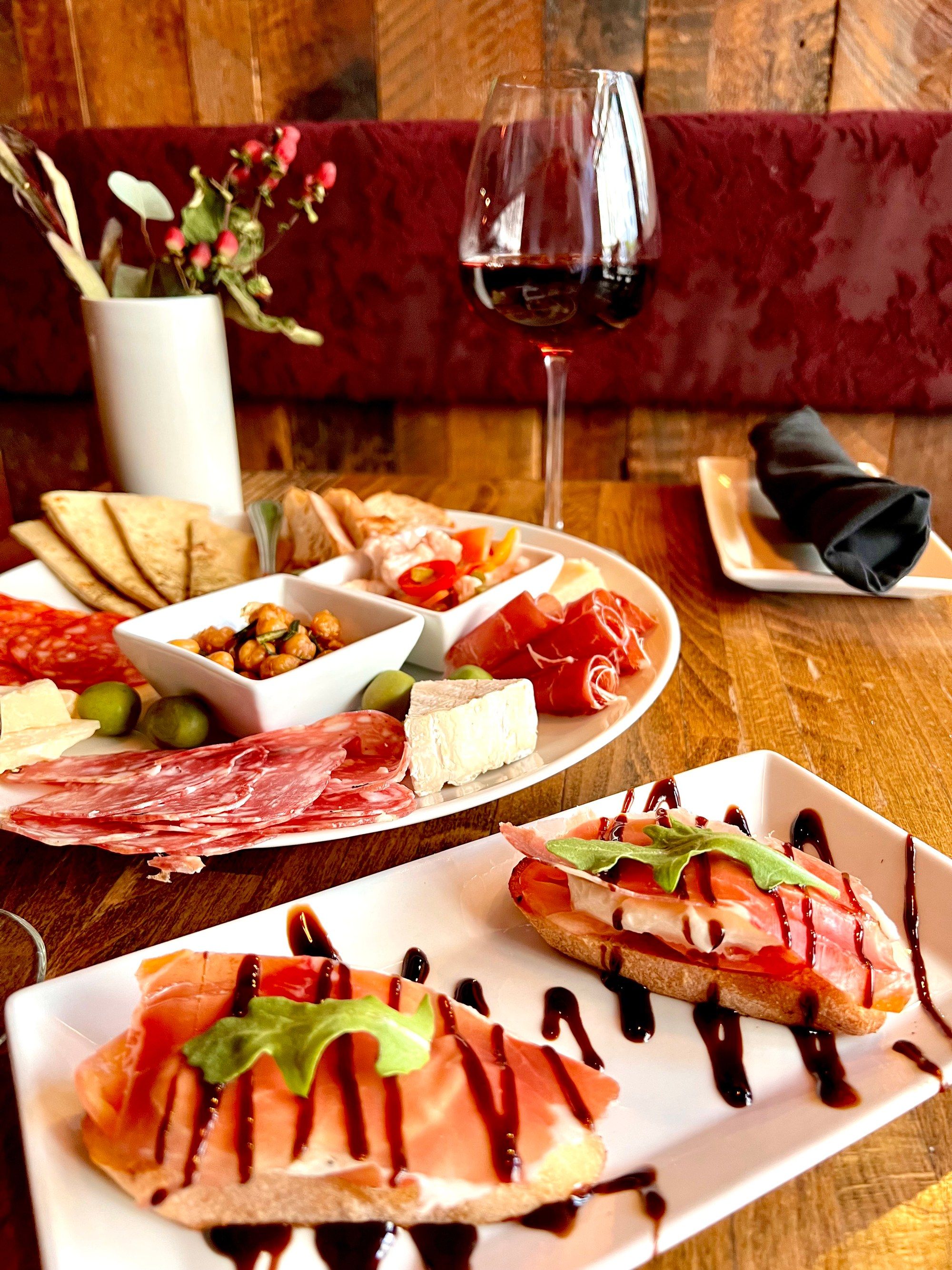 Charcuterie board with cured meats and cheese beside crostini and a glass of red wine