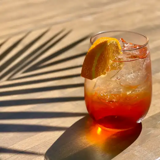 Amber cocktail with an orange slice in a stemless glass on a sunlit wooden table