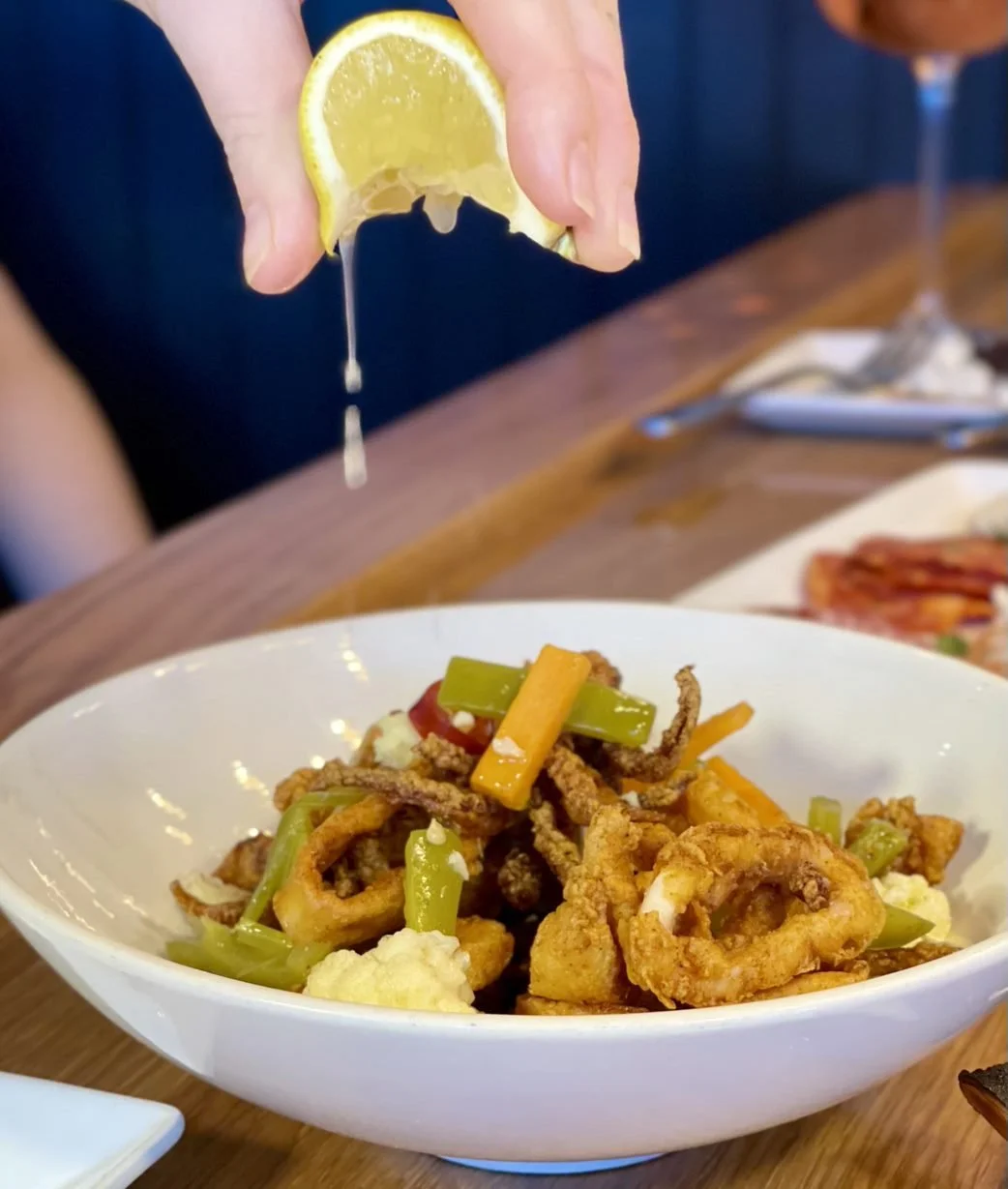 Hand squeezing lemon over a bowl of fried calamari with peppers and cauliflower