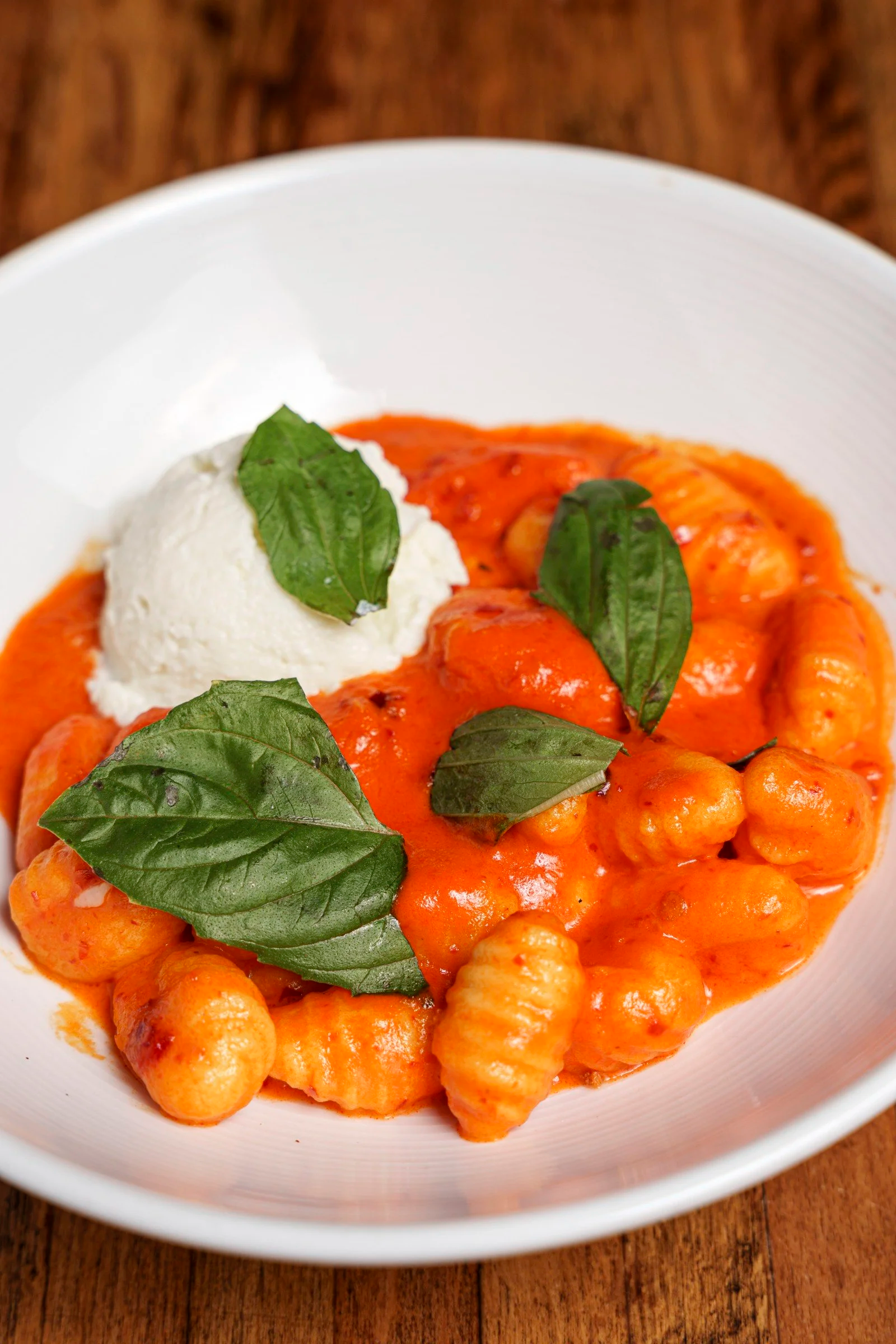 Bowl of gnocchi in red sauce with a scoop of white cheese and fresh basil leaves