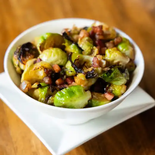 White bowl of roasted Brussels sprouts mixed with cubes of cured meat
