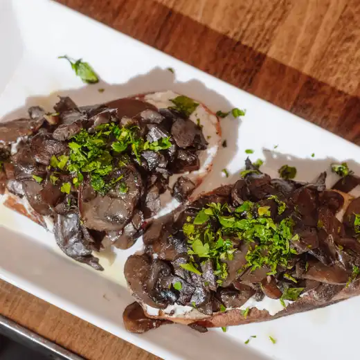 Two crostini topped with mushrooms, white spread and chopped parsley on a white plate