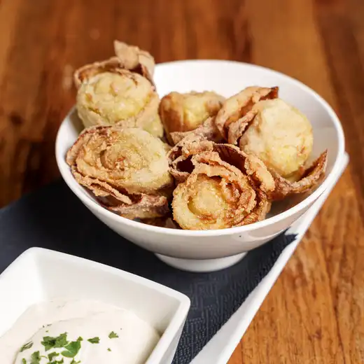 White bowl of fried artichokes beside a small dish of white dipping sauce