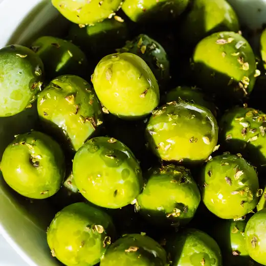 Close-up of green olives tossed with herbs in a white bowl