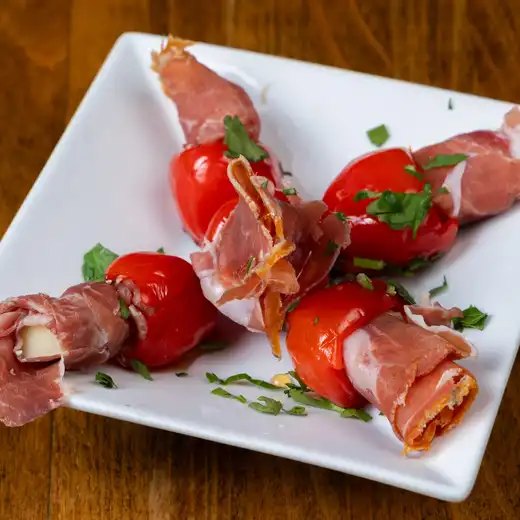 White plate with red peppers wrapped in cured meat and white cheese, garnished with parsley