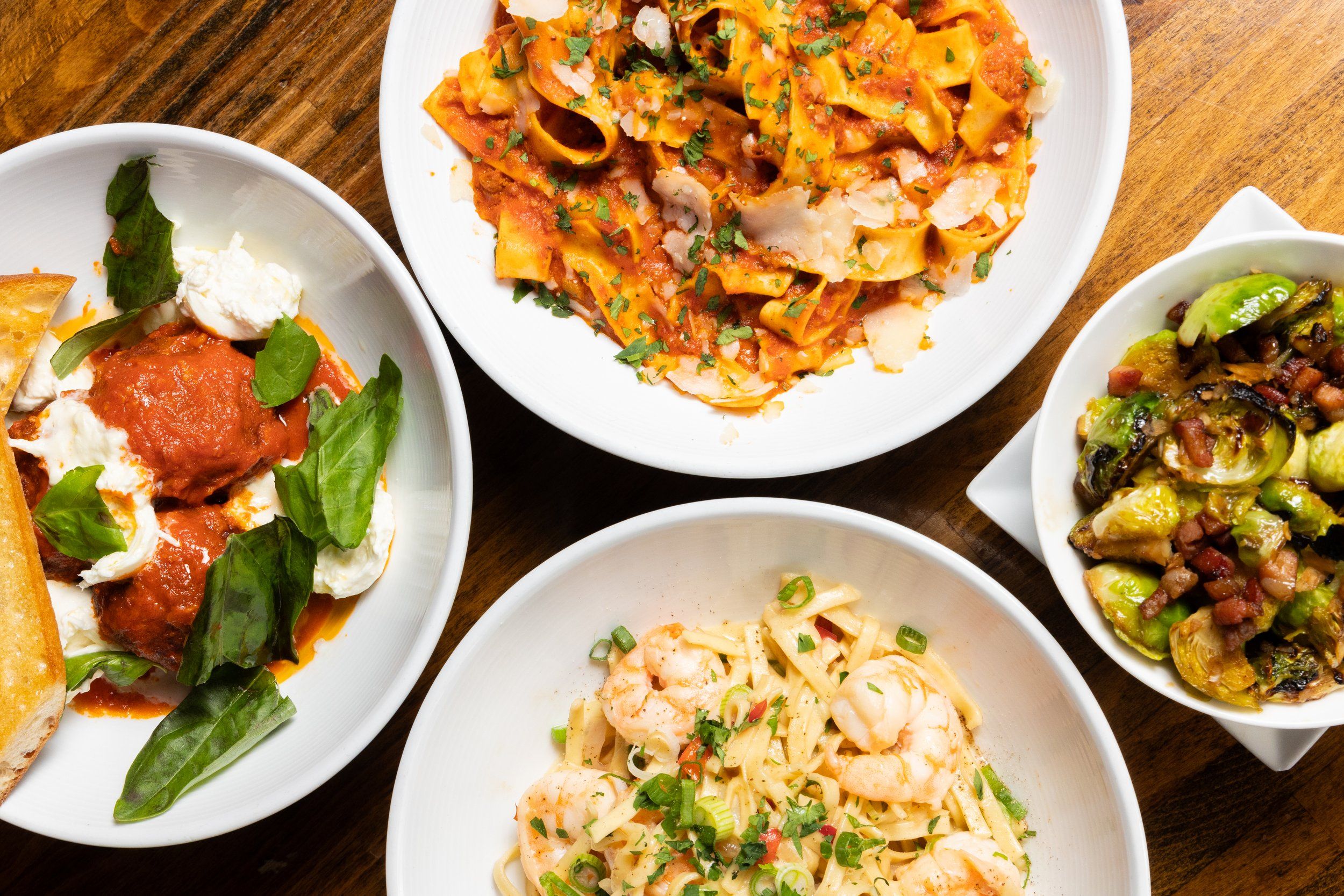 Spread of four Italian dishes: meatballs, pasta with red sauce, pasta with shrimp, brussels sprouts