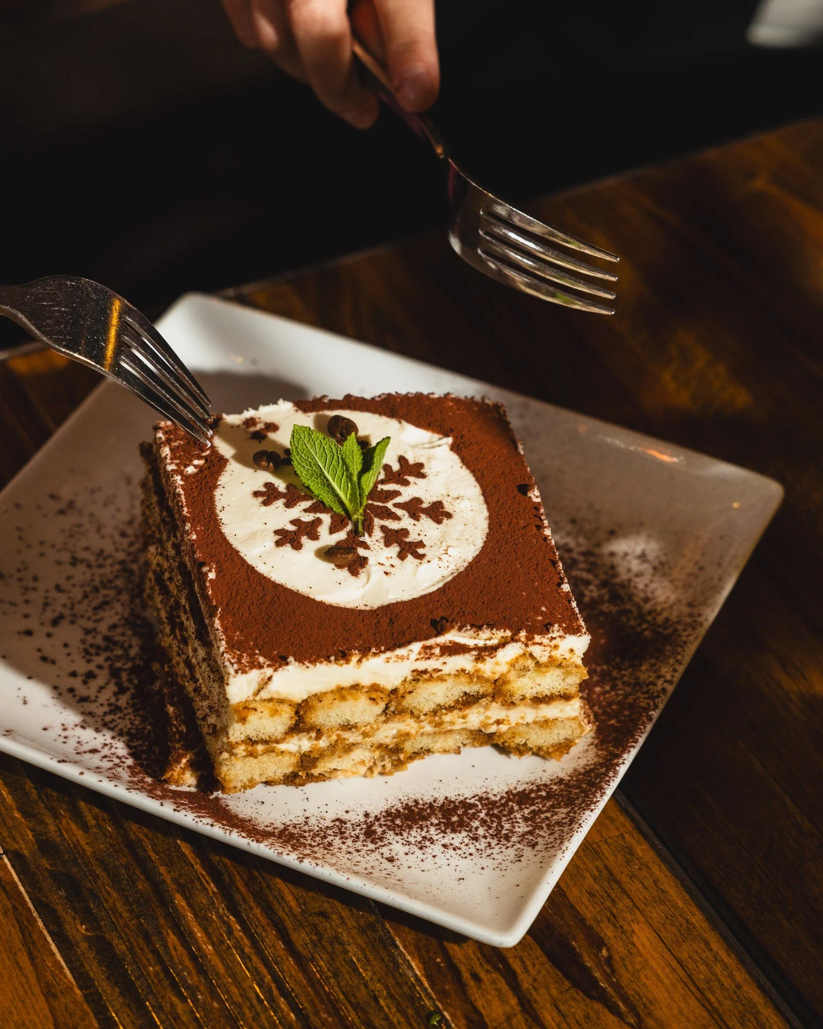 Rectangular Italian tiramisu plated on white with cocoa dusting