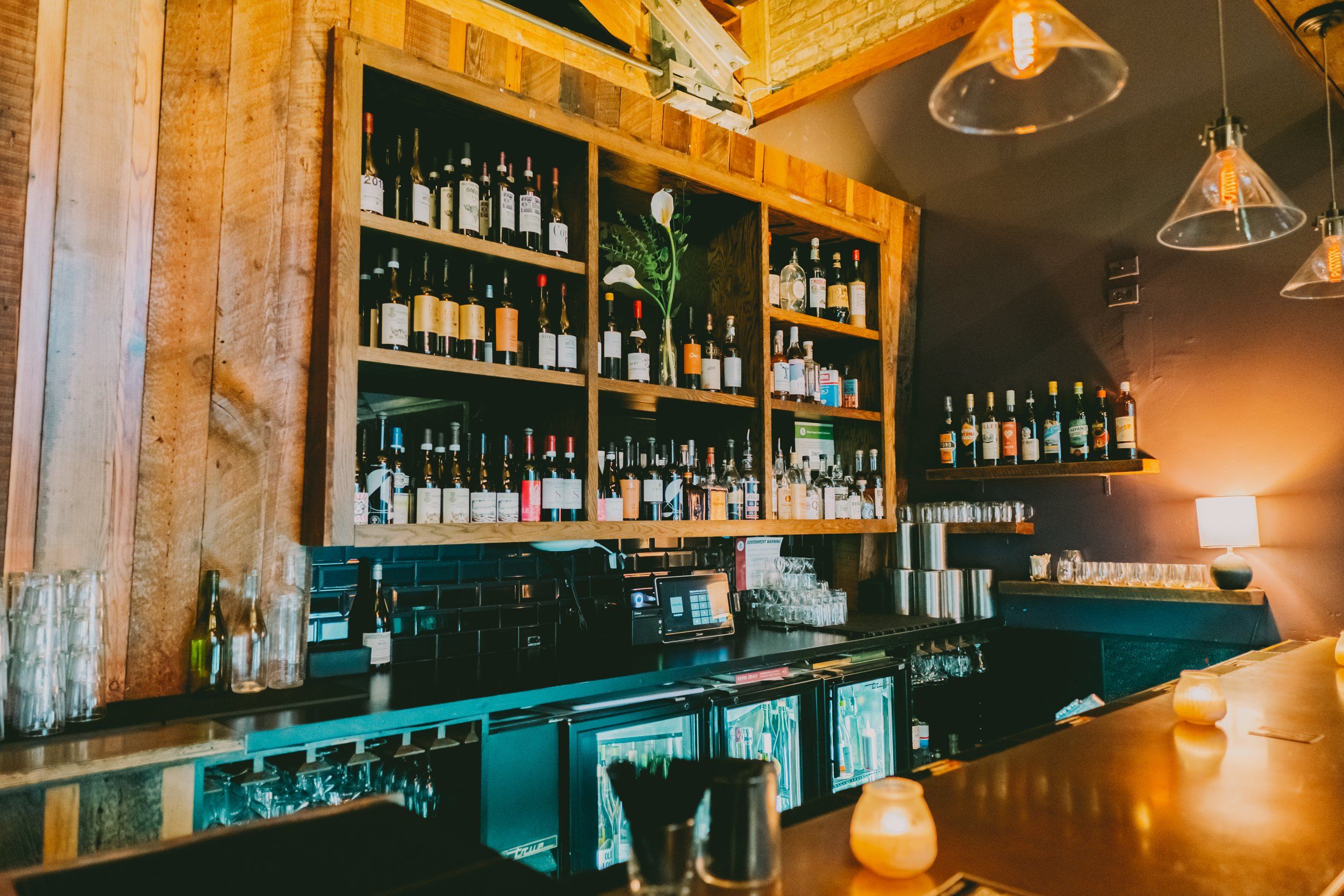 Wine bar interior with bottle-lined wooden shelves, hanging pendant lights, and bar counter