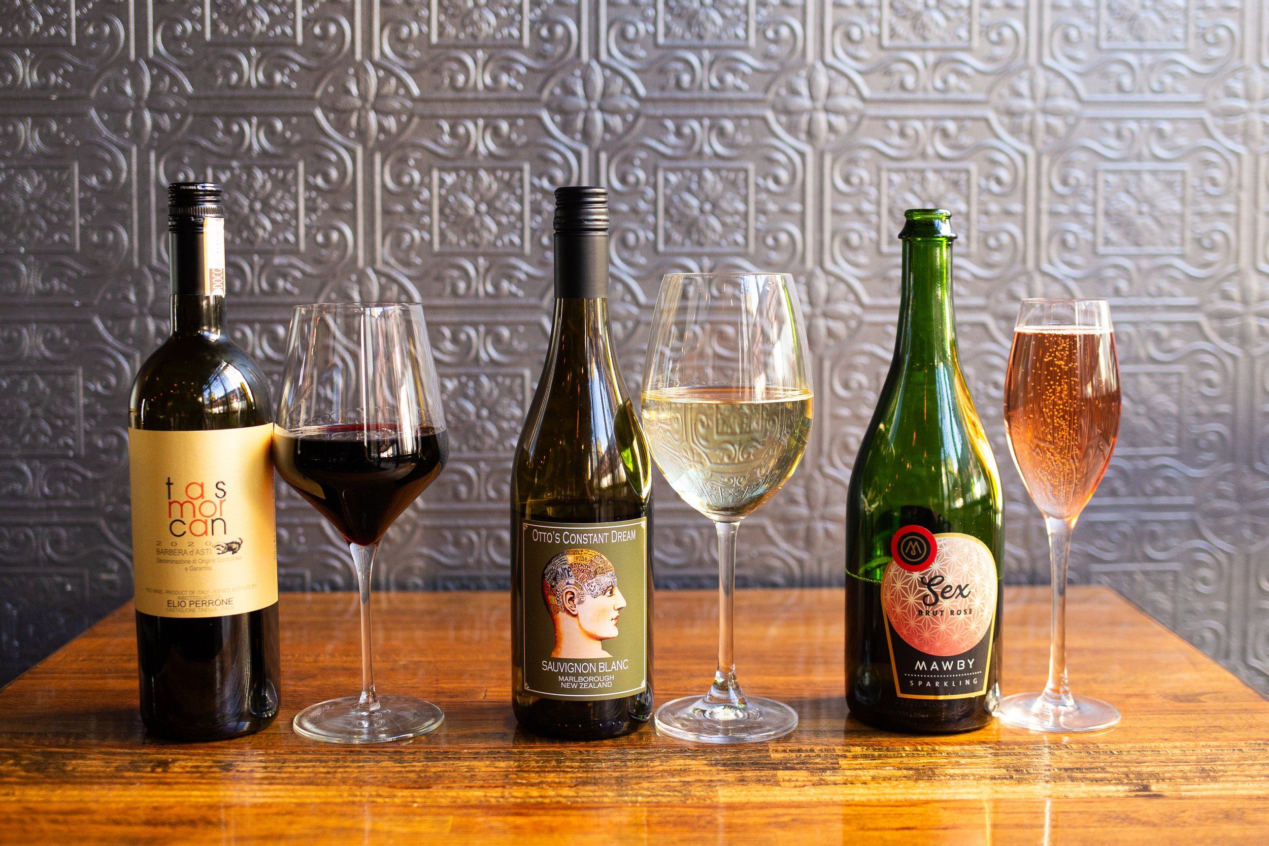 Three wine bottles paired with glasses of red, white and pink wine on a wooden table